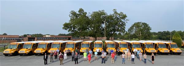 Ariel photo of transportation department standing in front of a row of new, yellow school buses.